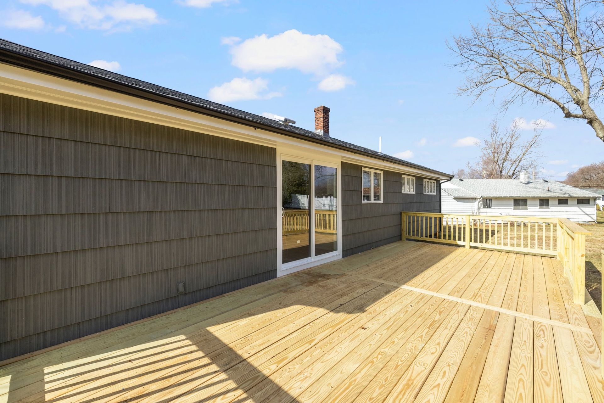 Wooden deck outside a house with gray siding and a sliding glass door.