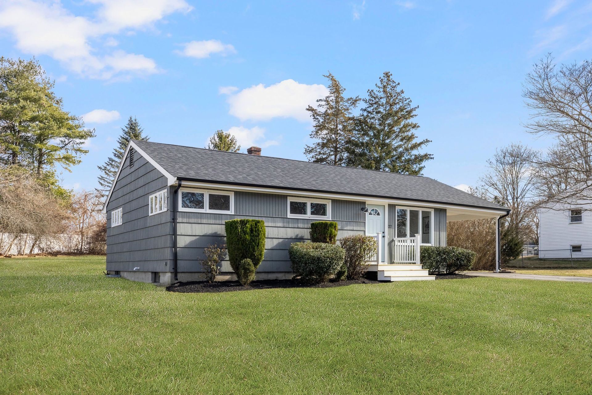 Gray ranch-style house with green lawn, blue sky, and bushes in front.