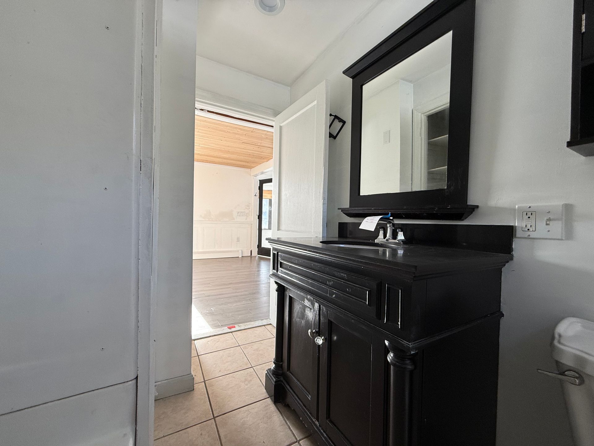 Bathroom with black vanity, mirror, and open doorway to another room.