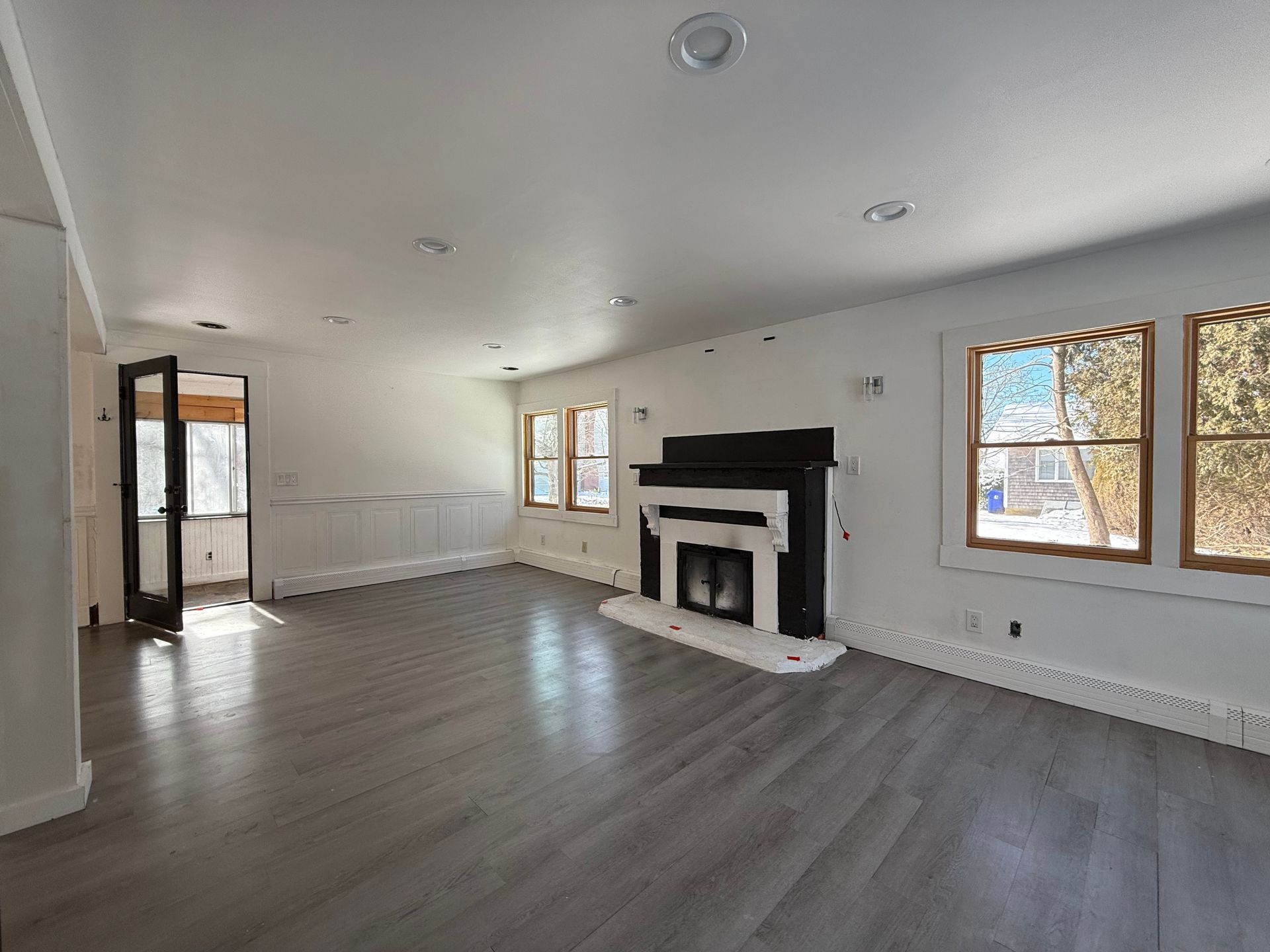 Empty living room with wood flooring, fireplace, and windows; white walls and trim.
