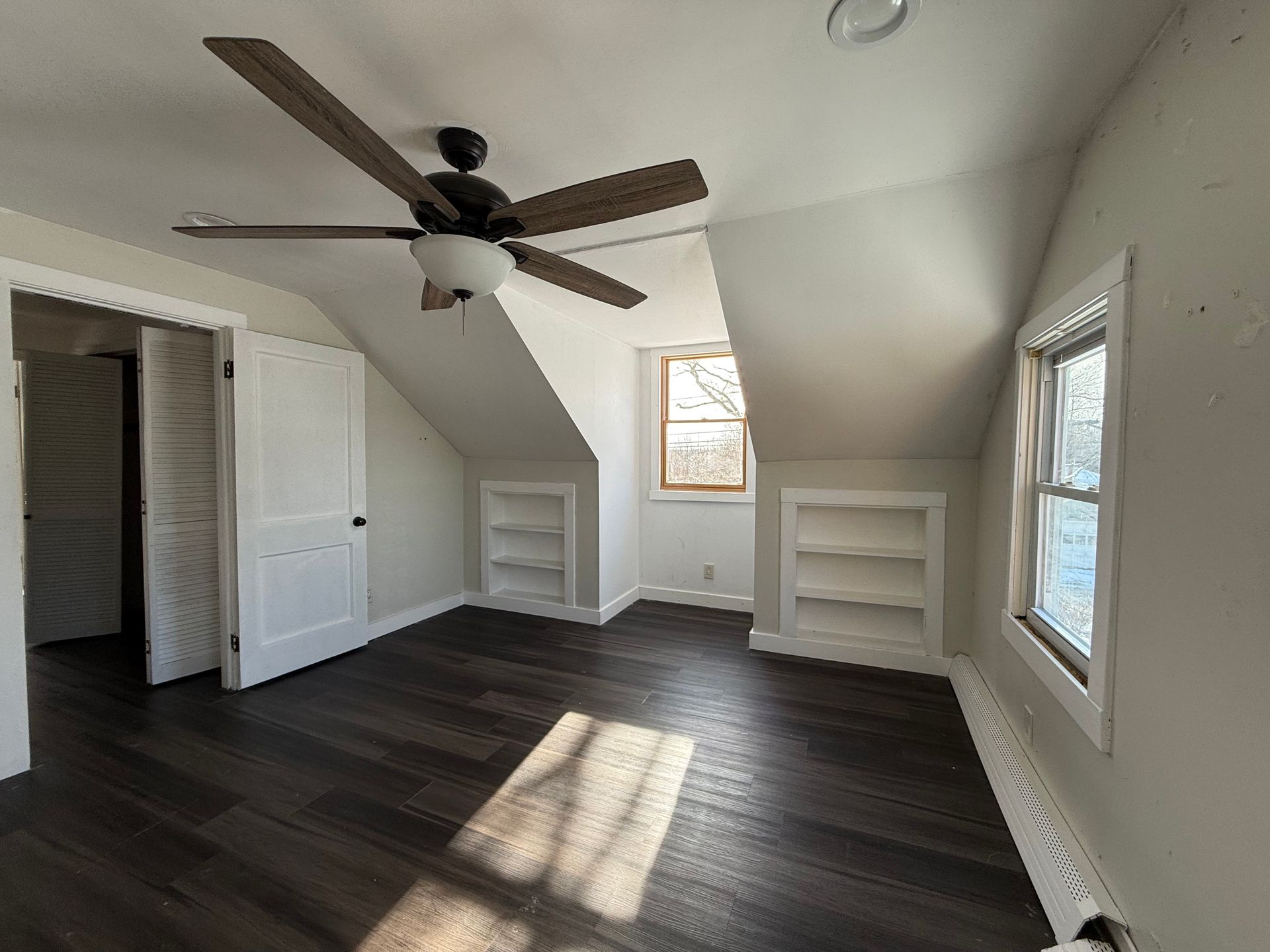 Bedroom with dark wood floors, white walls, built-in shelves, and a ceiling fan.
