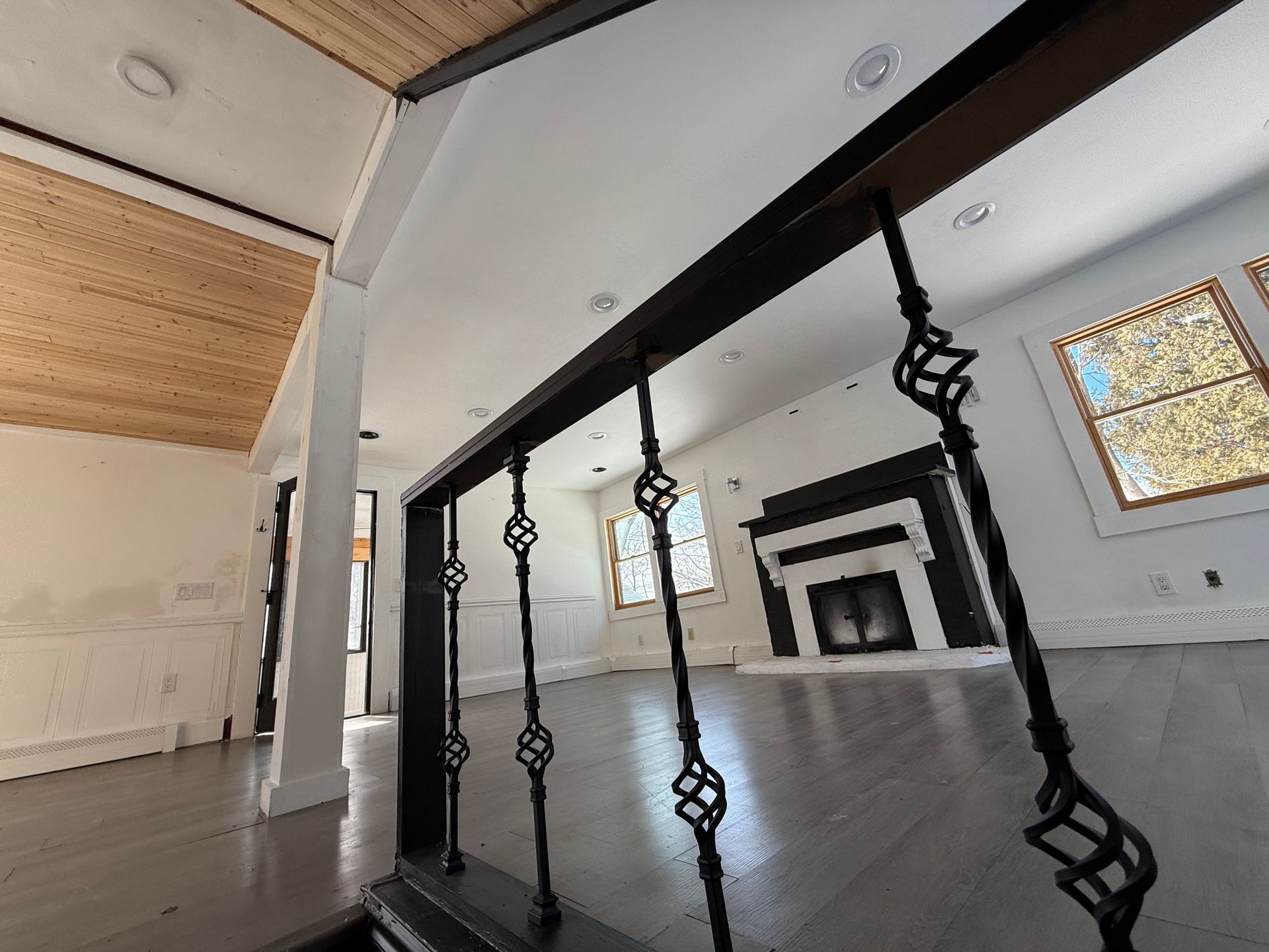 Black iron railing in home; wood ceiling and white walls; fireplace visible in background.