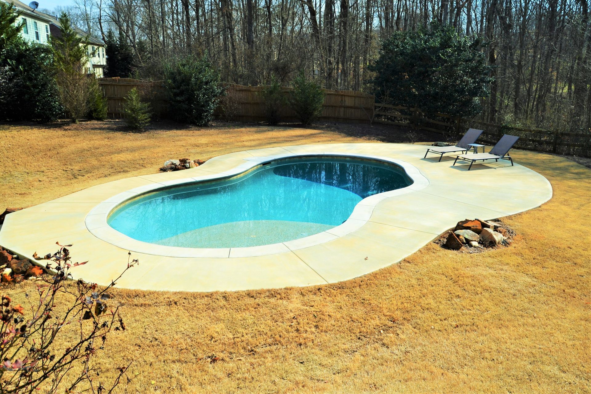 A large swimming pool is surrounded by chairs in a backyard.