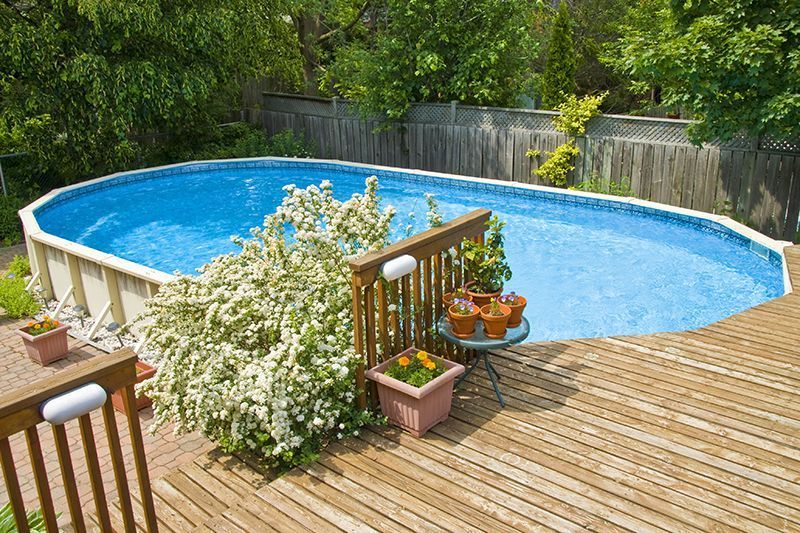 A large swimming pool is sitting on top of a wooden deck.