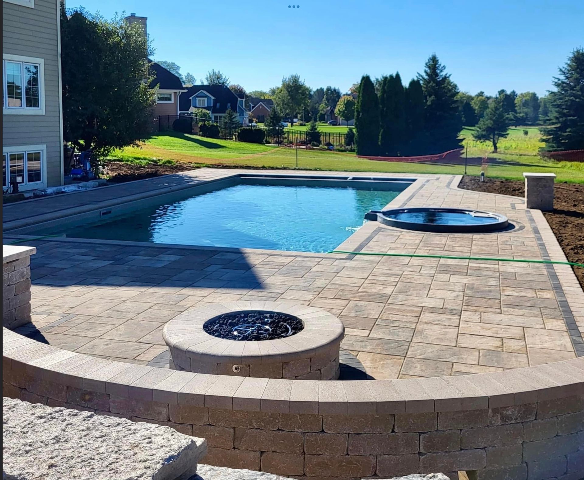 Backyard patio with pool, hot tub, and fire pit on a sunny day.