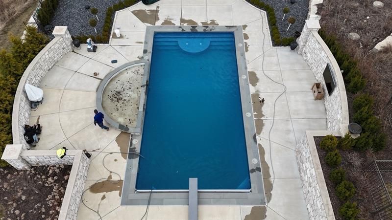 Aerial view of a rectangular pool with a dark blue surface, surrounded by concrete and stone walls.