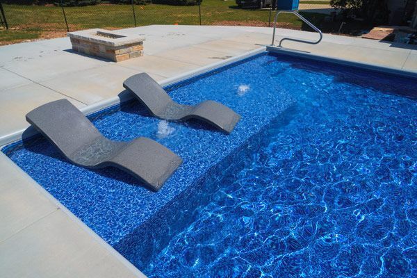 Swimming pool with two gray chaise lounge chairs. Blue water and a concrete deck.