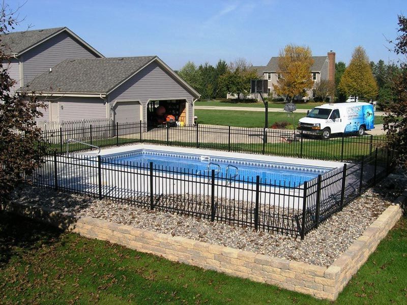 Rectangular backyard pool with black fence and service van in a residential setting.