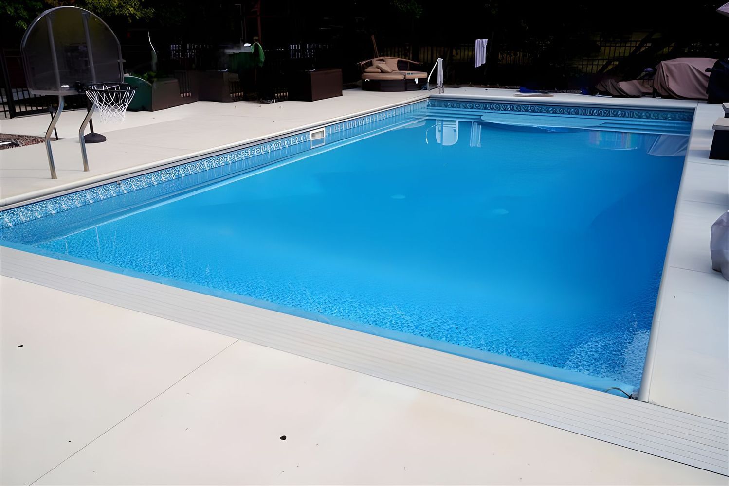 Rectangular swimming pool filled with blue water, surrounded by light-colored concrete.
