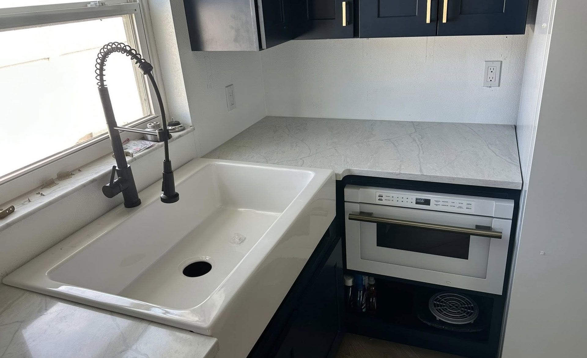 Kitchen corner with sink, faucet, countertop, microwave, and cabinets.