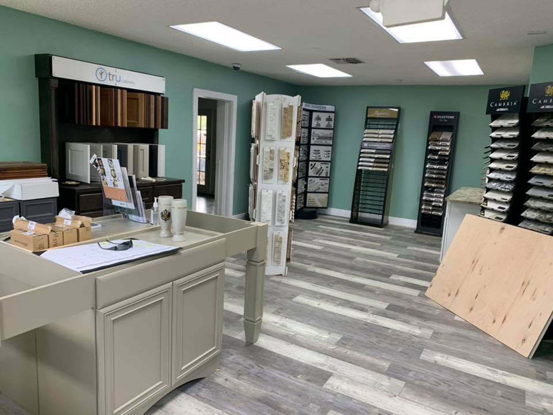Interior of a showroom with cabinet and flooring samples on display. Light blue walls, light wood-look floor, and a display counter.