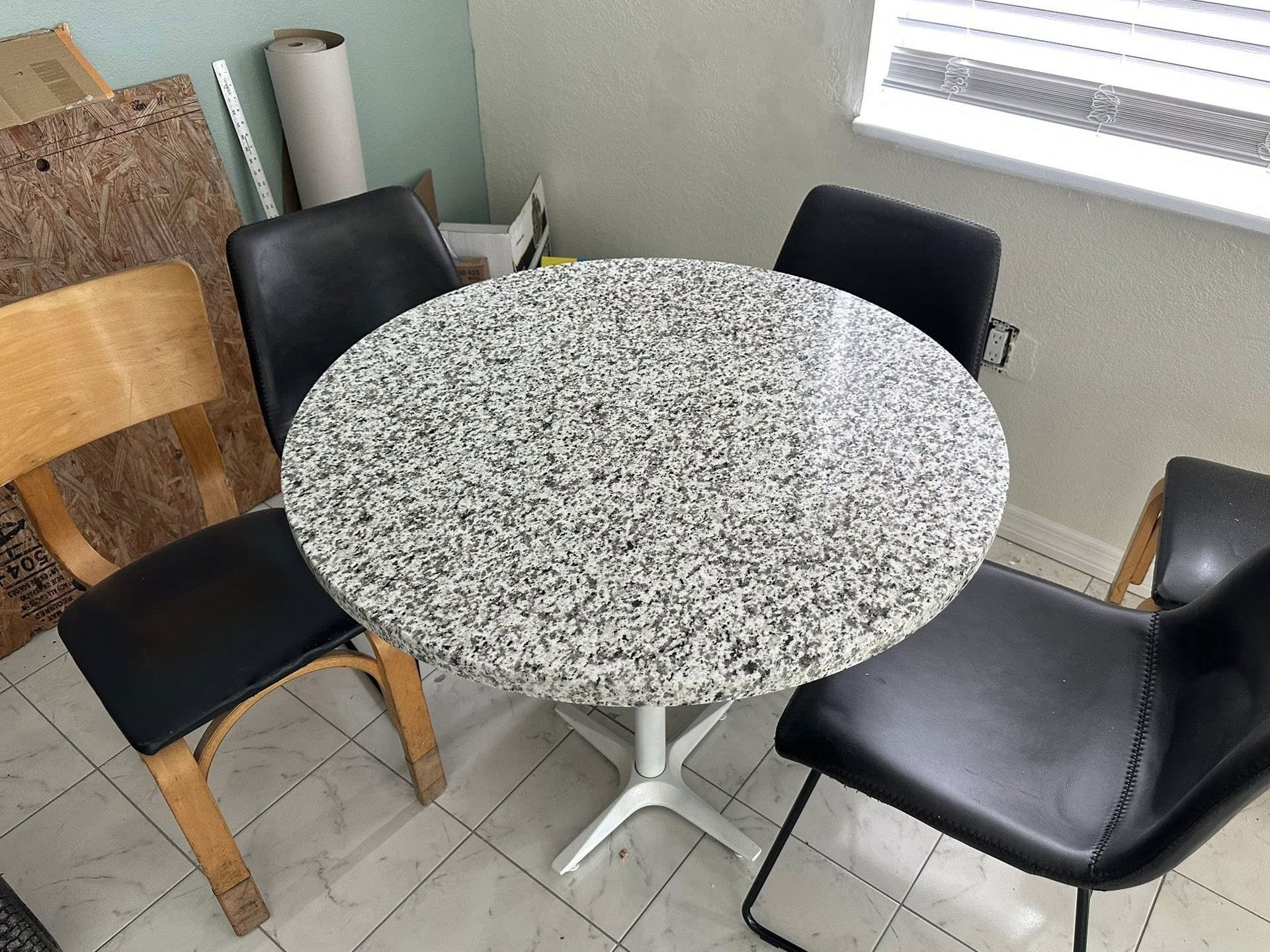 Round table with speckled top, surrounded by three black chairs and one wooden chair.