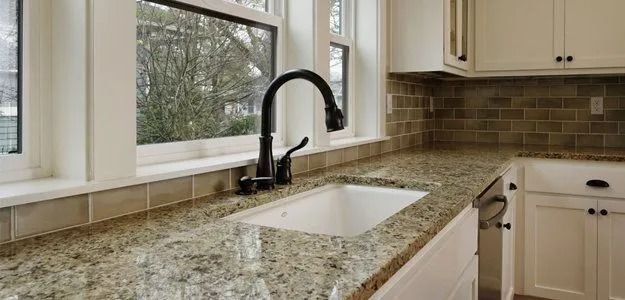 Kitchen sink with a view of a window. Dark faucet and light-colored countertops. Cabinets in the background.