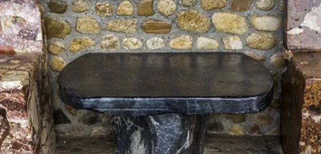 A dark stone table with rounded edges is set in a stone alcove. The background is a rock wall.