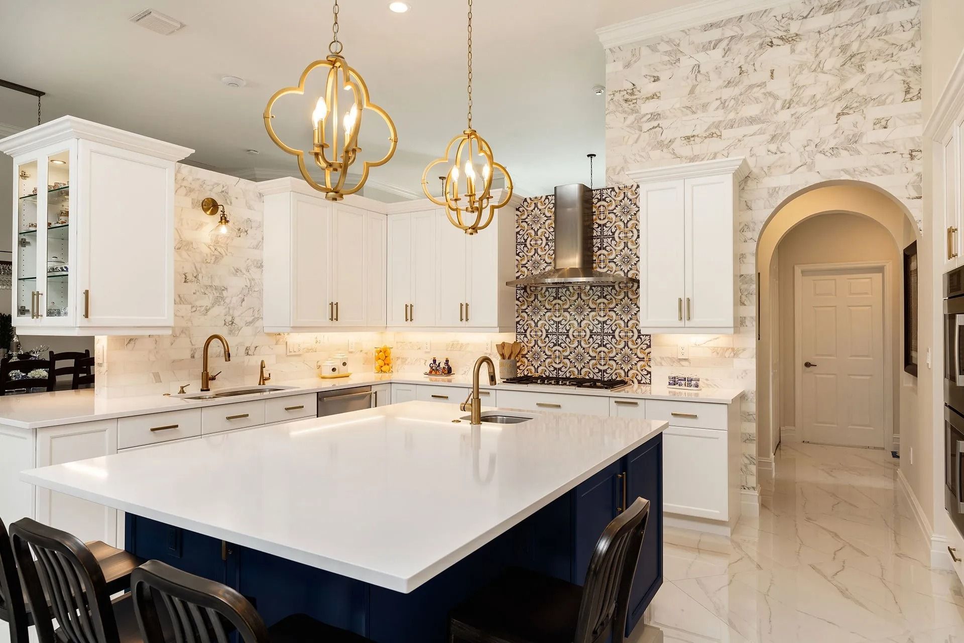Elegant white kitchen with blue island, gold light fixtures, and marble accents.