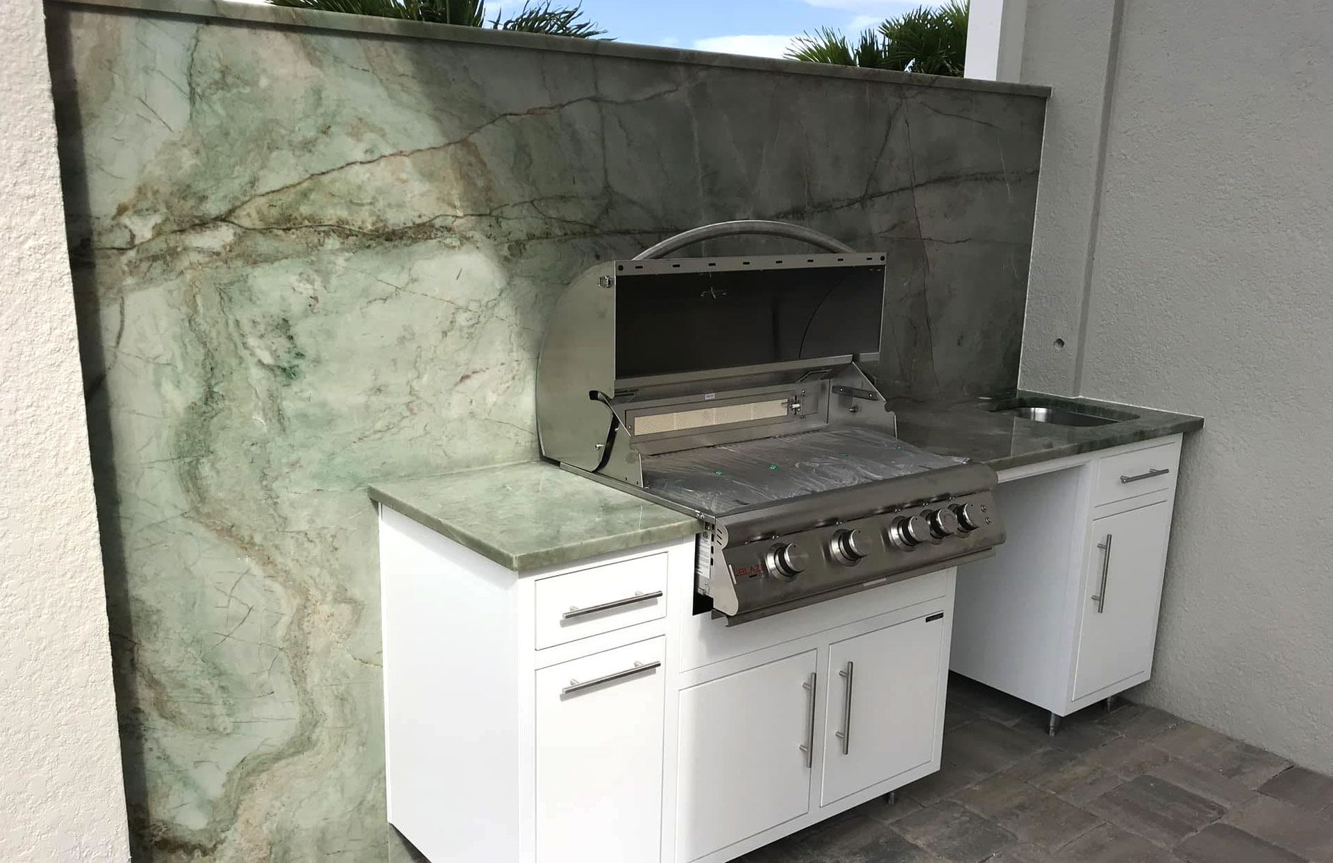 Outdoor kitchen with white cabinets, built-in grill, and green marble backsplash.