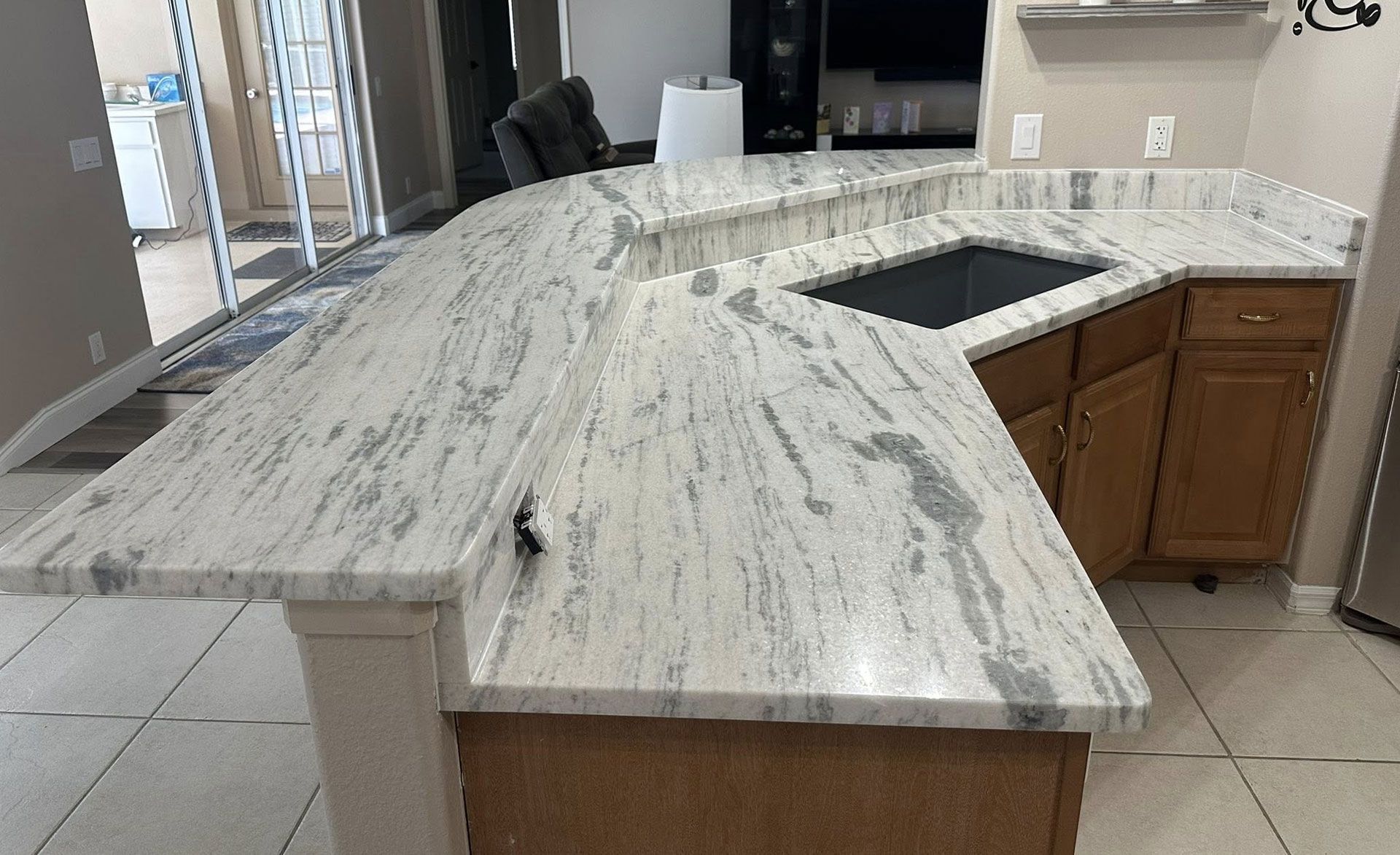 A granite countertop curves over wooden cabinets. The sink is black, and a white pillar supports the counter.