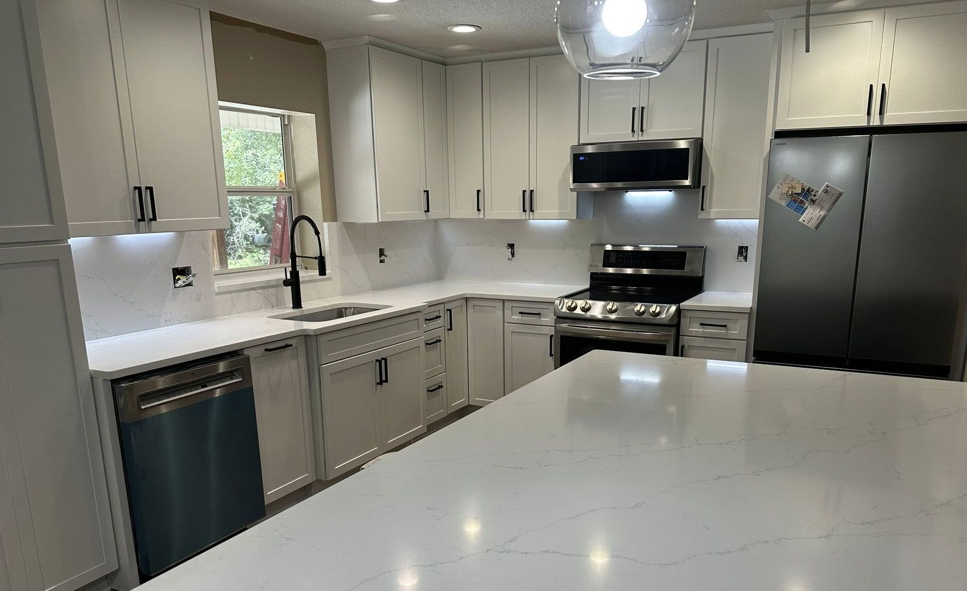 White kitchen with island, cabinets, stainless steel appliances, and dark hardware.