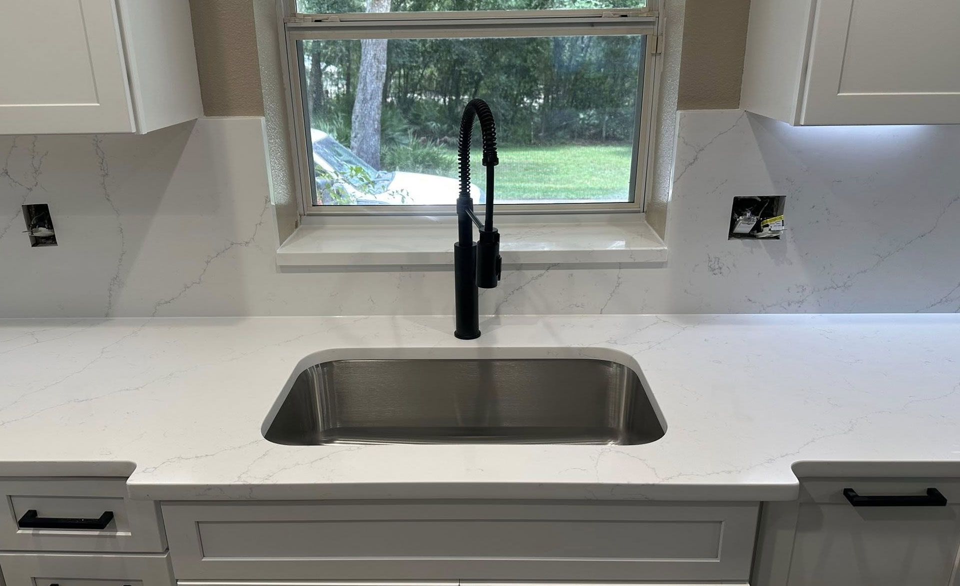 Kitchen with white cabinets, quartz countertop, stainless steel sink, black faucet, and window.