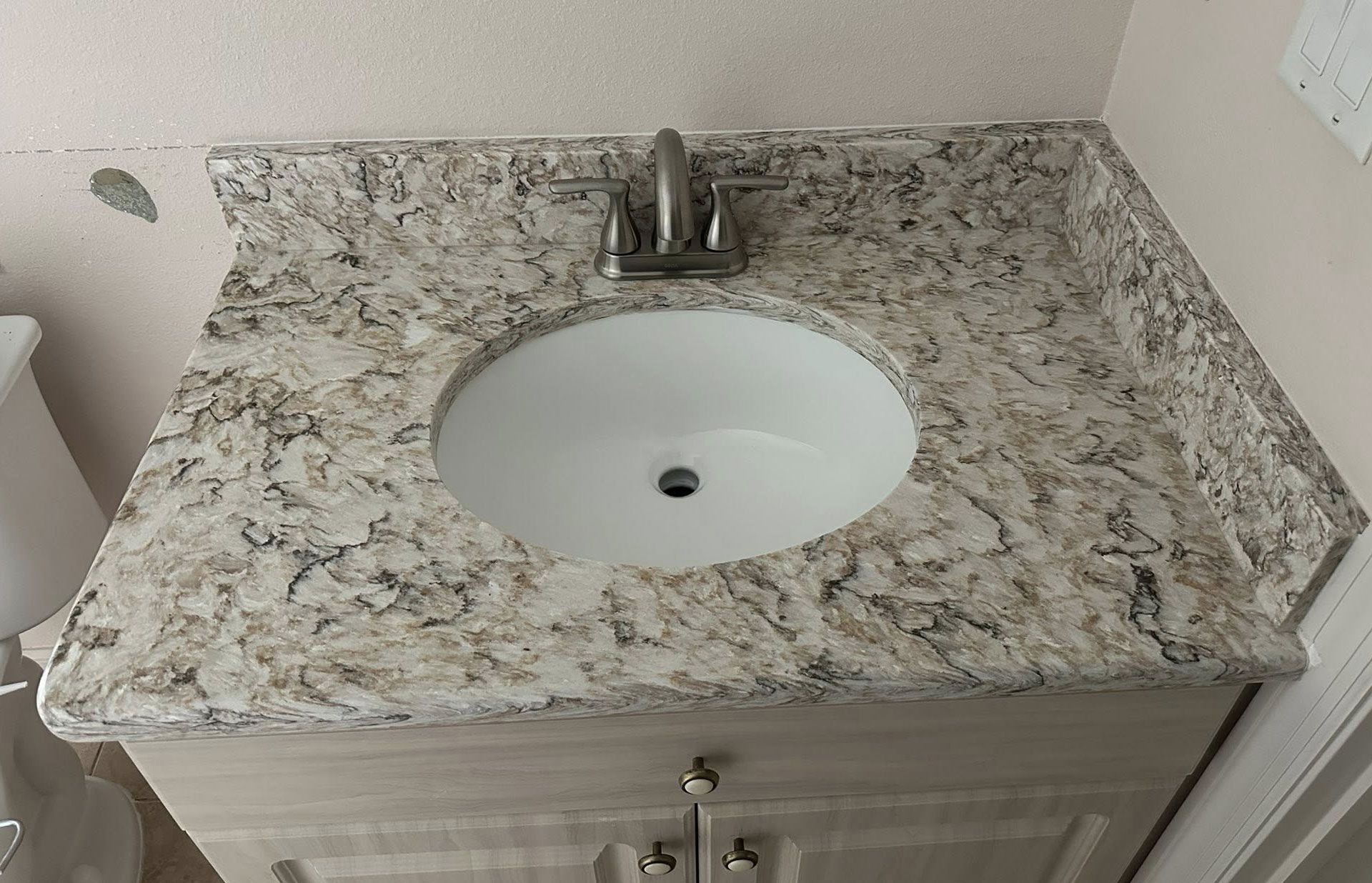 Bathroom vanity with oval sink, light countertop, silver faucet, and light-colored cabinet with two doors.