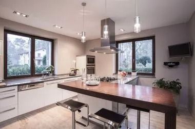 Modern kitchen with island, white cabinets, and stainless steel appliances. Black windows overlook greenery.
