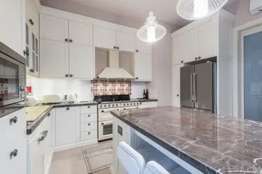 White kitchen with marble countertop island, white cabinets, stainless steel appliances, and two hanging lights.