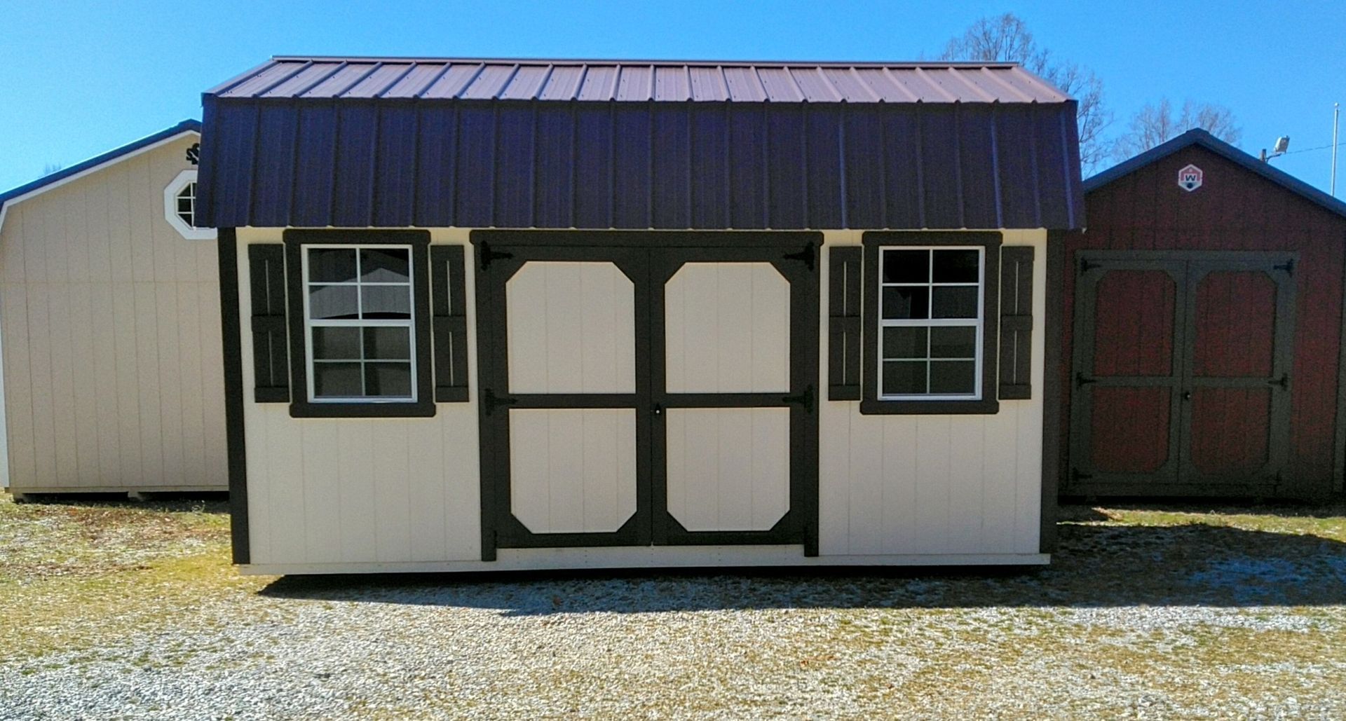 A small shed with shutters on the windows is sitting next to a garage.