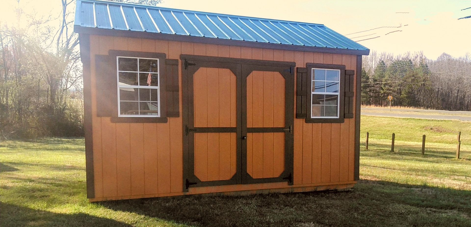 A small orange shed with a blue roof is sitting in the middle of a grassy field.