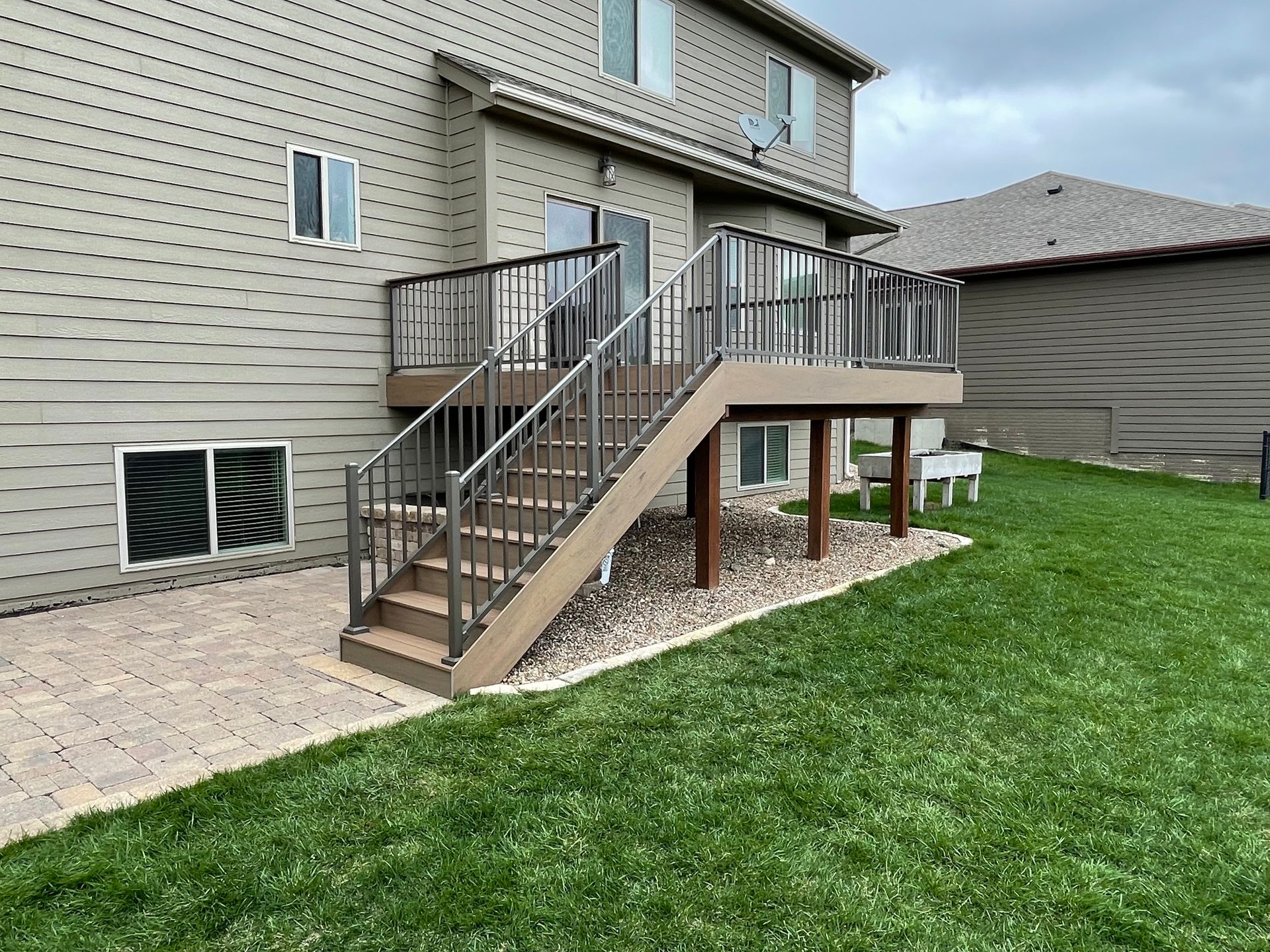 A two-story house with a composite deck and stairs leading to a green backyard.
