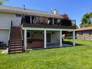 Backyard deck with stairs, black railing, hot tub, and green lawn.