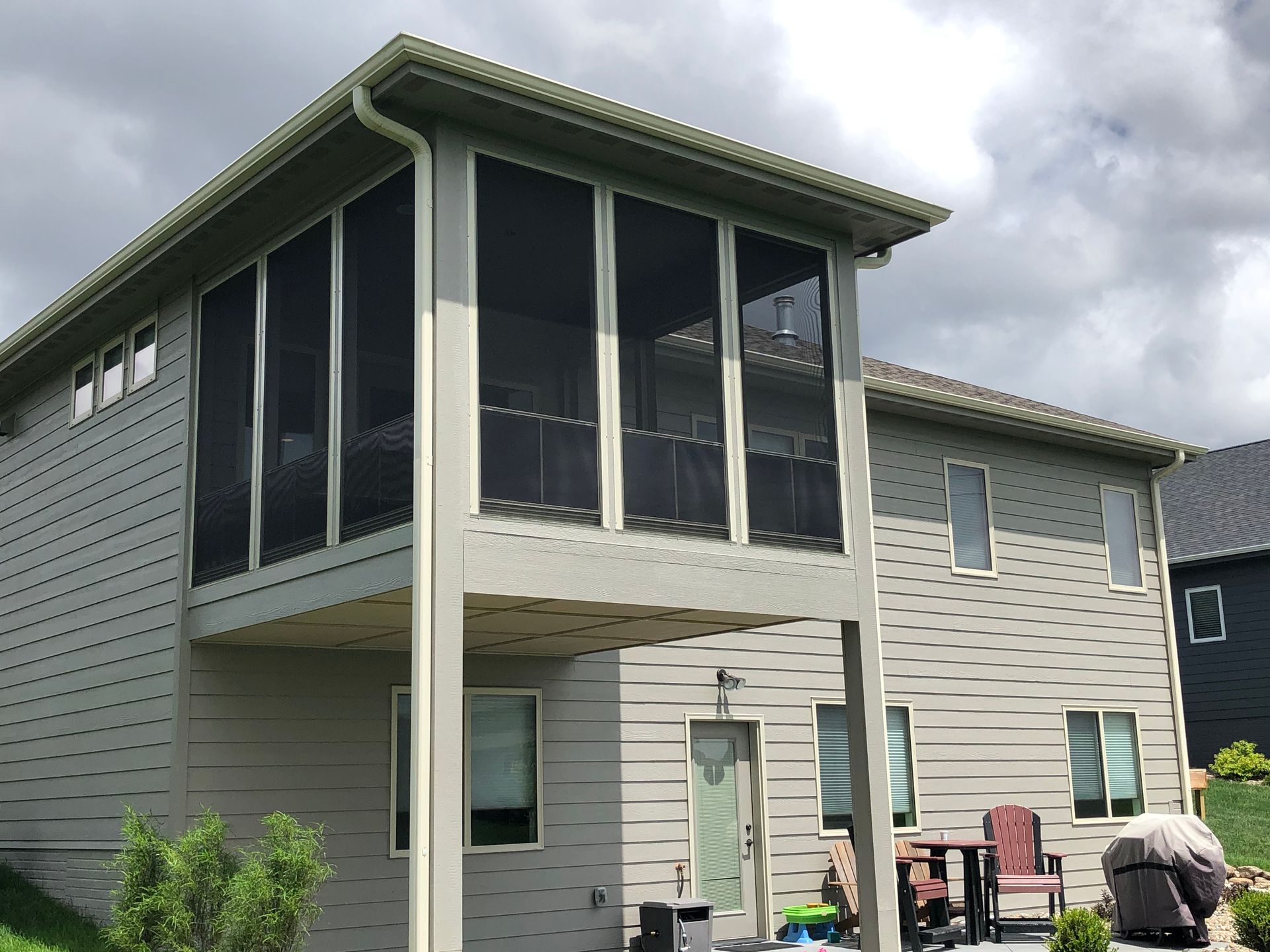 Two-story house with a screened-in porch on the upper level. Beige siding, dark screens, overcast sky.