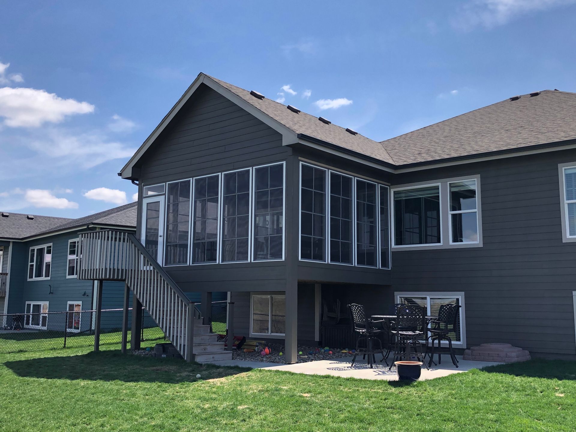 A house with a screened porch and deck, gray siding, blue sky, and a green lawn.