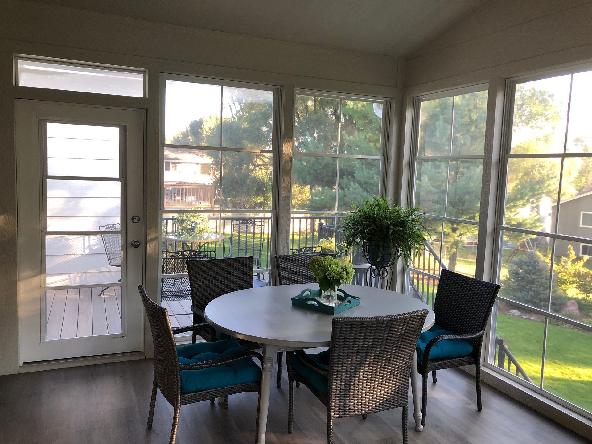 A sunroom with a round table and chairs, surrounded by windows overlooking a yard.