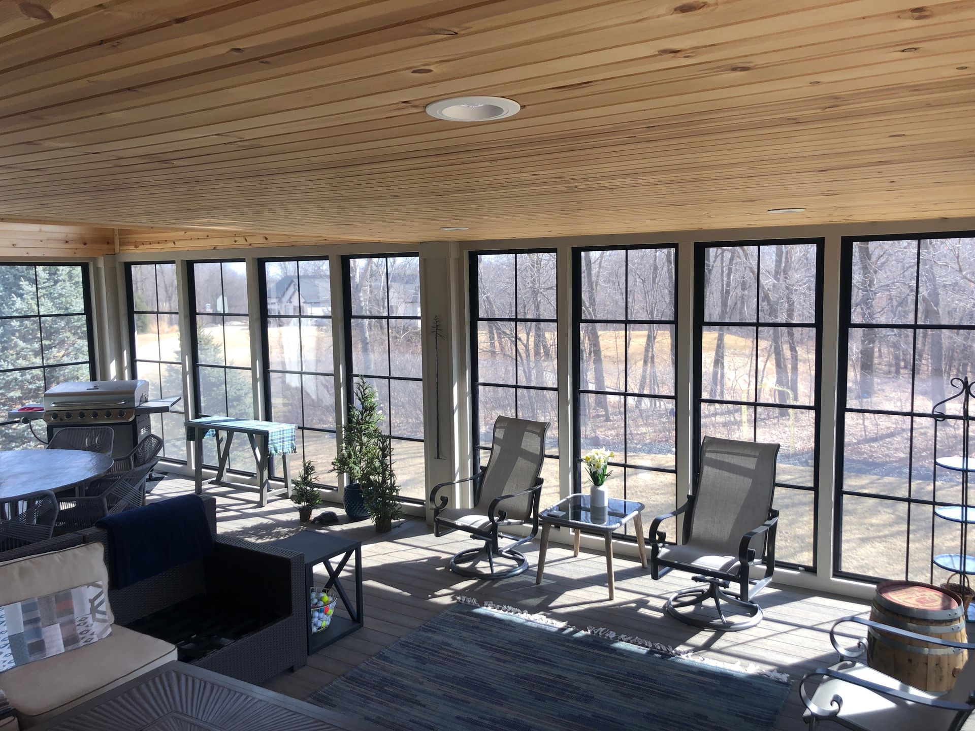 Sunroom with large windows, furniture, and wooden ceiling. Natural light fills the space.