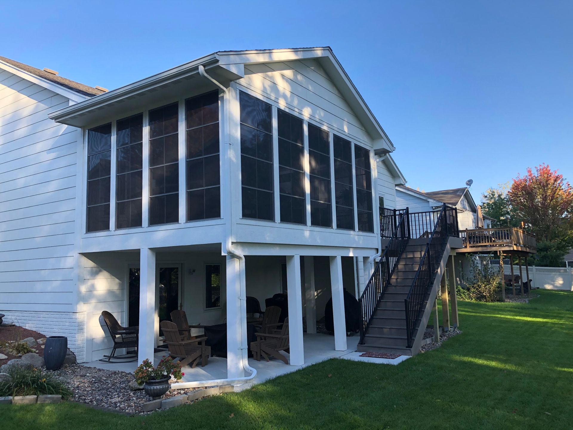 White two-story screened porch with chairs. Black stairs lead to a second story deck. Green grass.