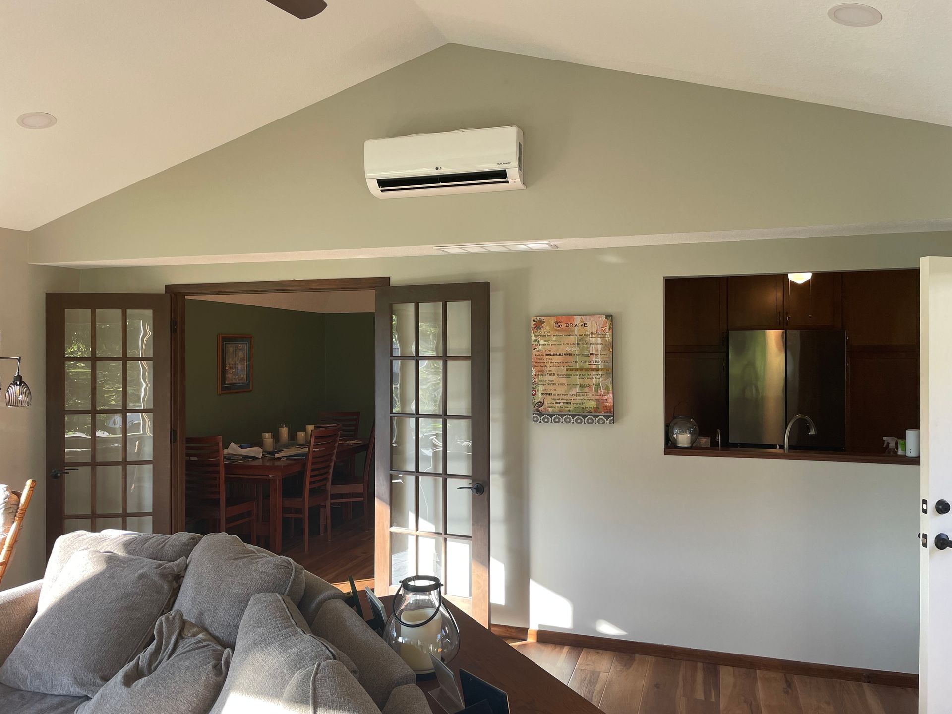 Interior of a room with French doors, a sofa, and an air conditioner. Olive-green walls and hardwood floors.
