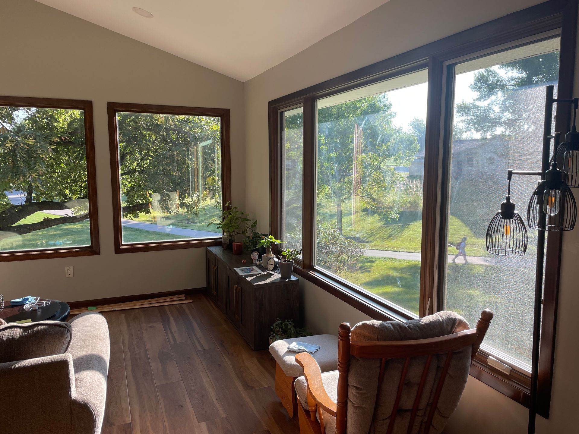 Sunroom with large windows overlooking a green yard. Dark wood trim, plants, and a sitting chair.