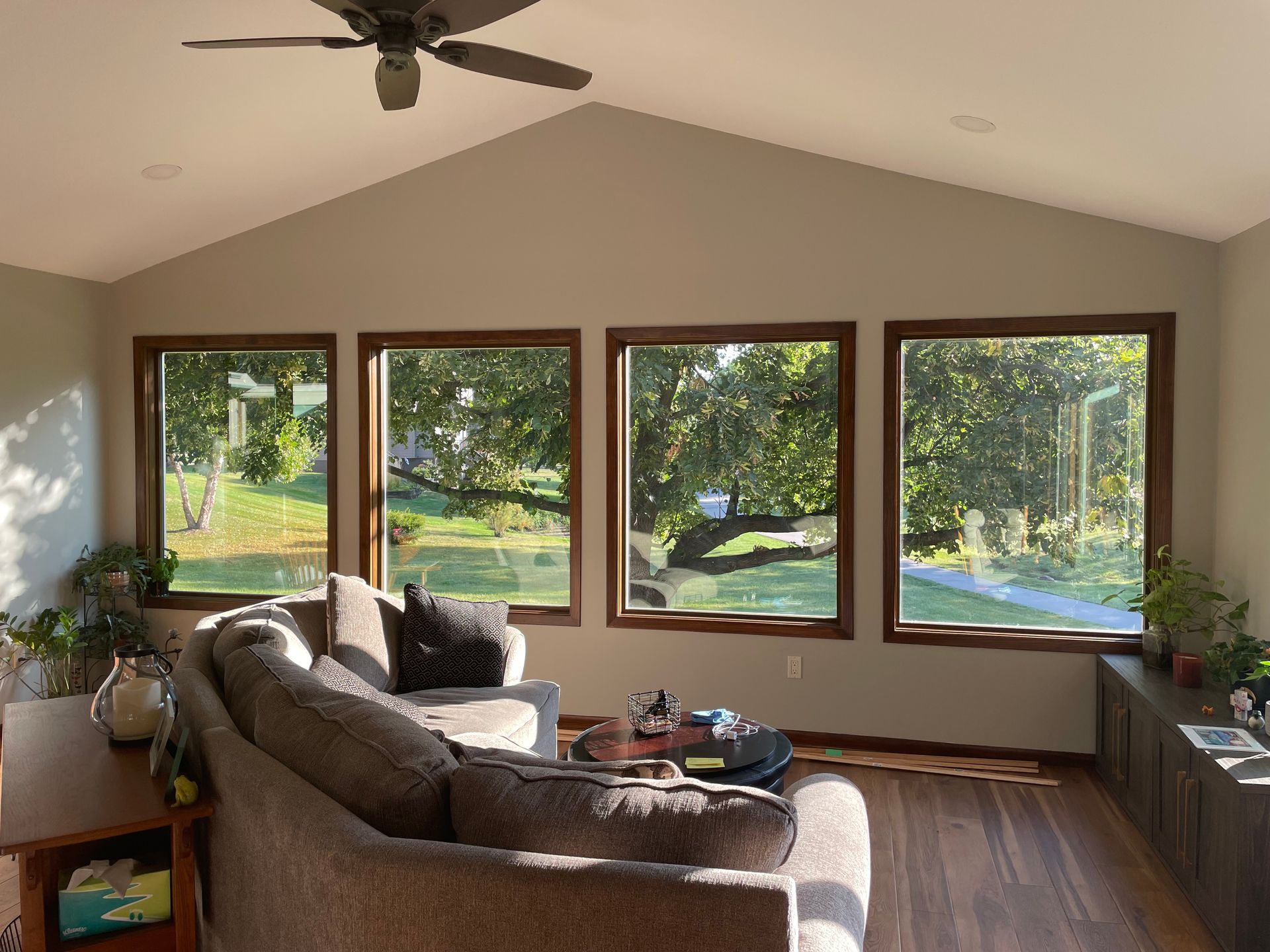 A living room with large windows and a brown couch facing outdoors with a green lawn and trees.