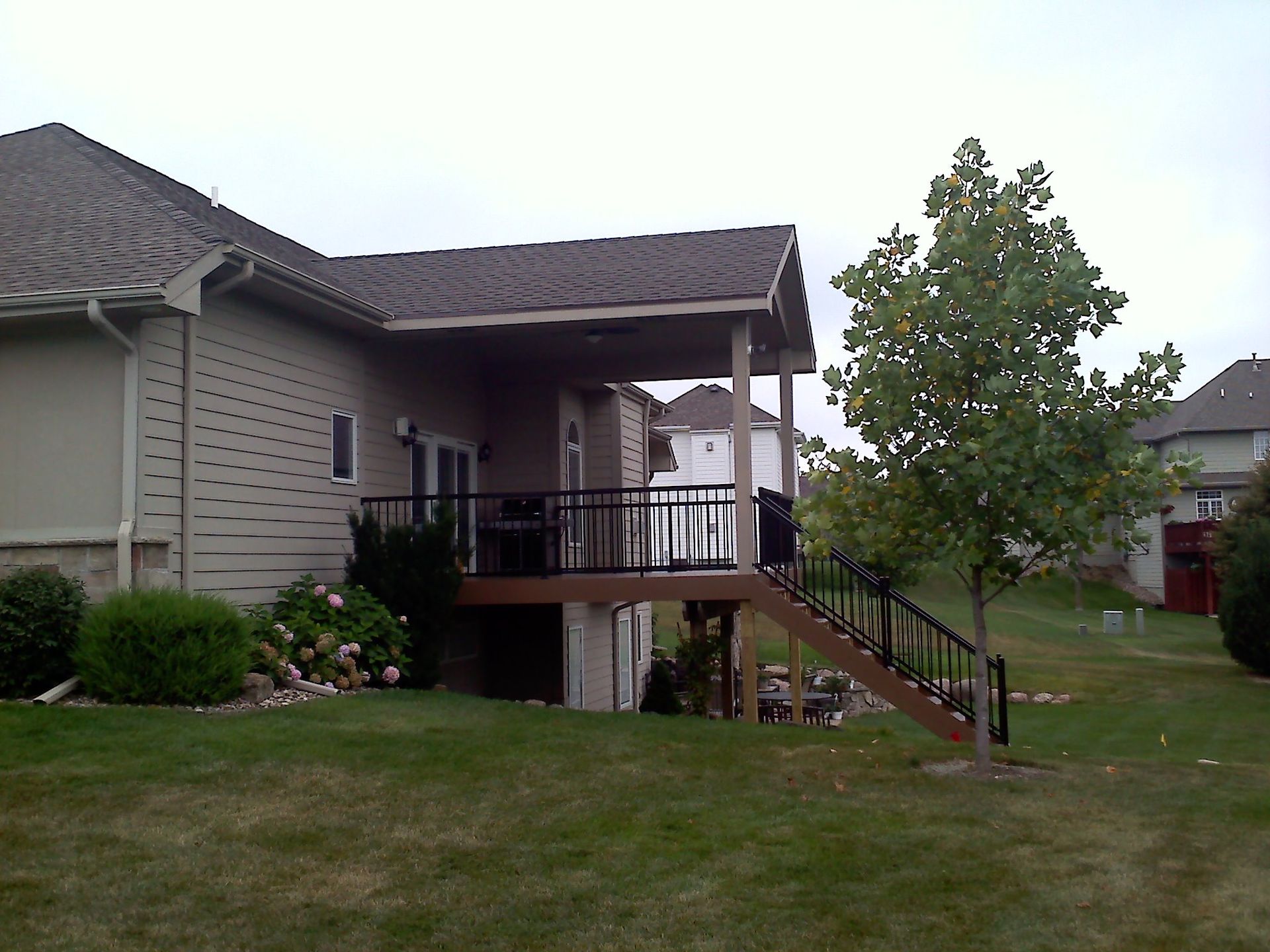 Backyard with a covered deck, stairs, and a small tree on a cloudy day.