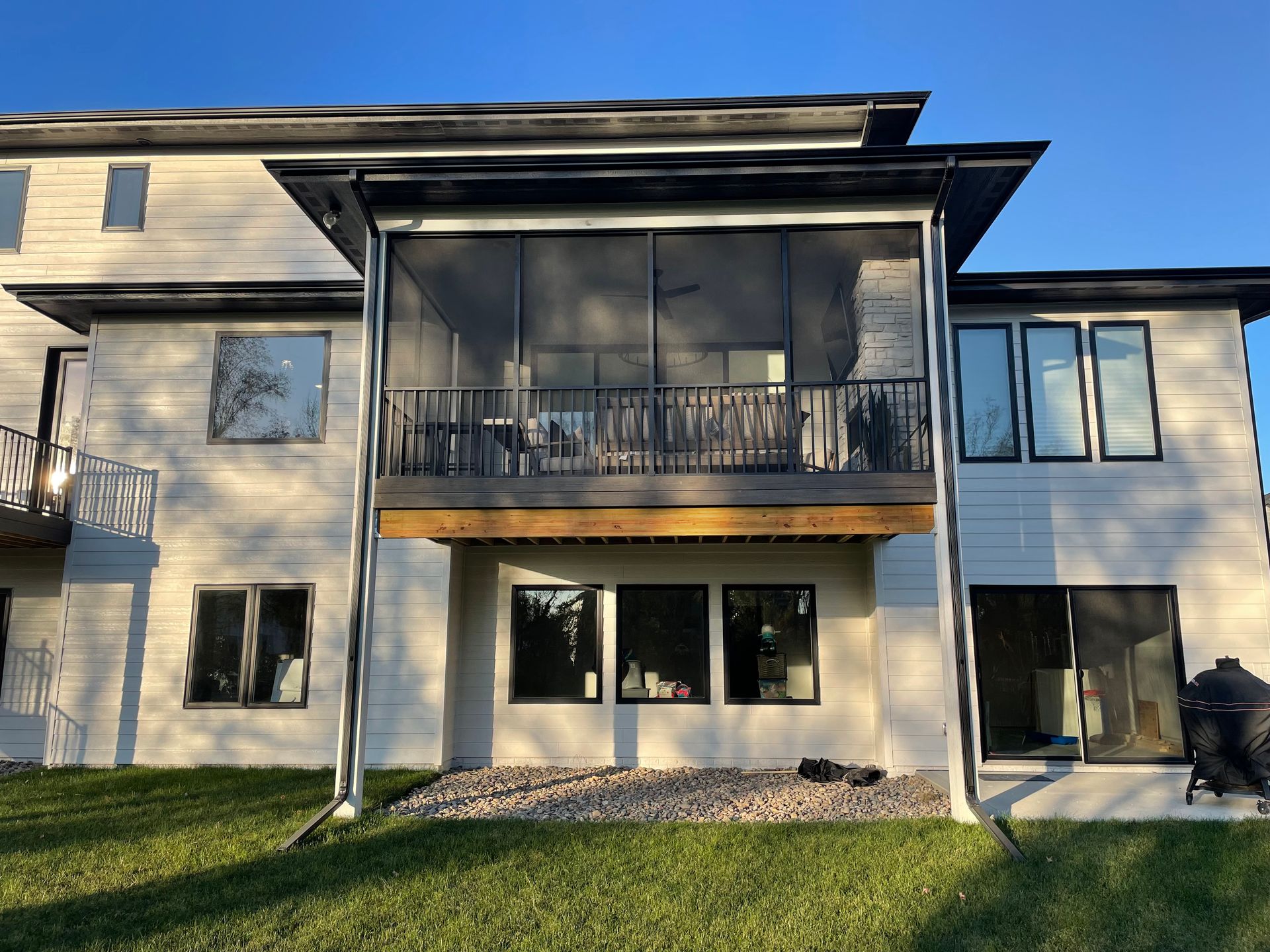 Back of a two-story white house with a screened-in porch, large windows, and a grassy yard.