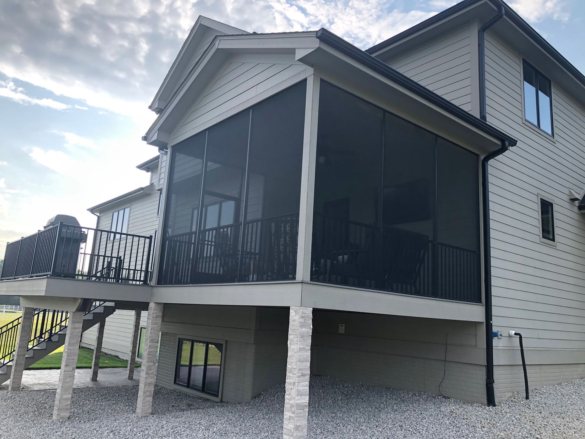 Screened-in porch attached to a two-story house with black railing and beige siding.