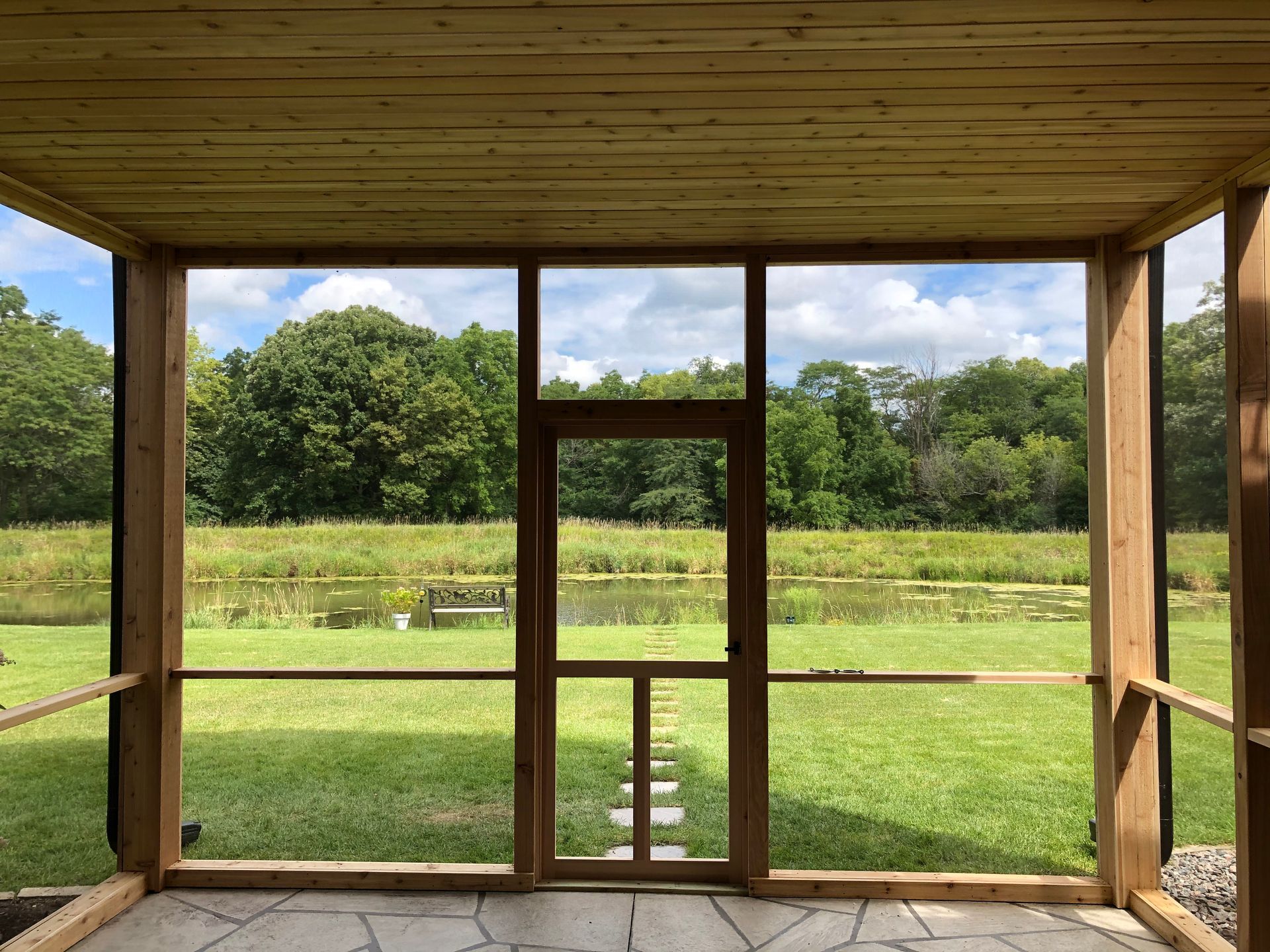 Screened porch with view of green lawn, pond, and trees.
