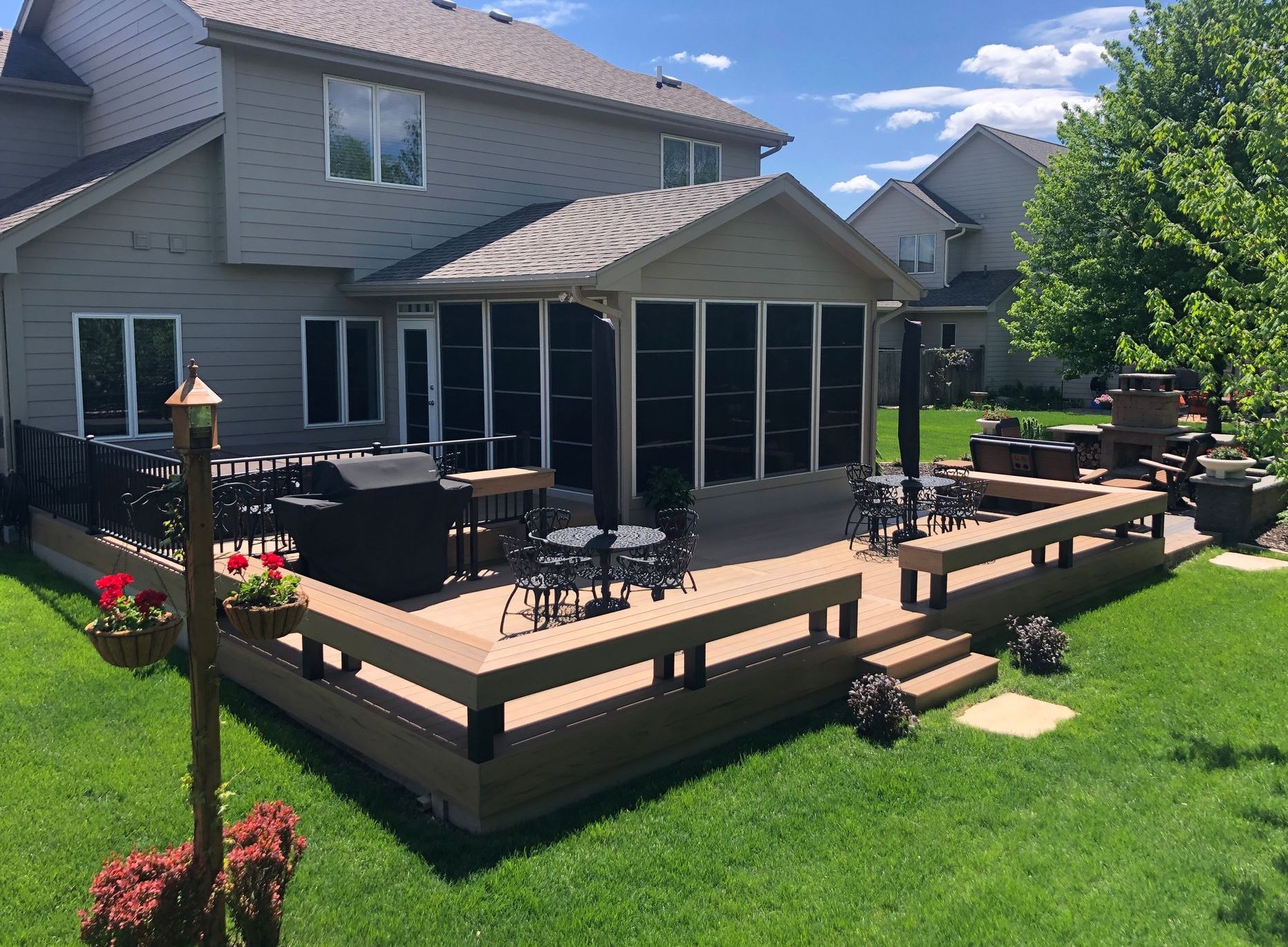 Backyard deck with screened-in porch. House with light siding and green lawn. Outdoor furniture and grill.