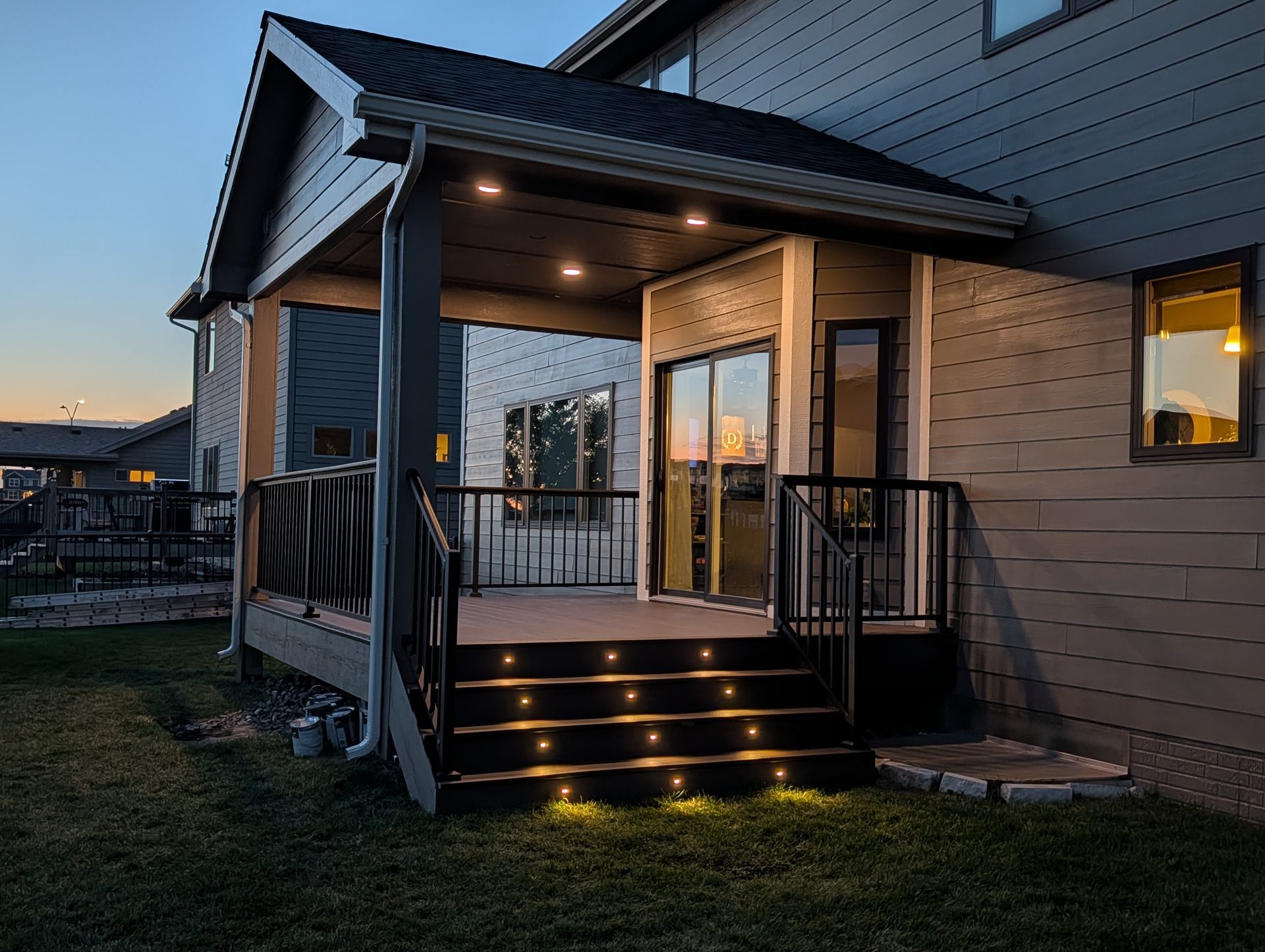 Lit outdoor deck with steps, a covered area, and a house at dusk.