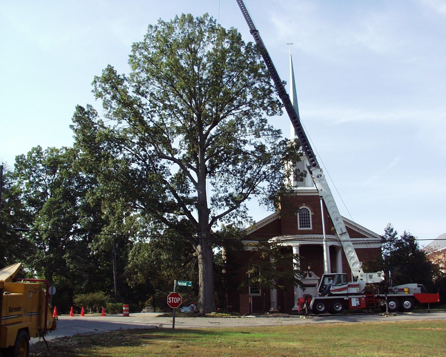 Fire truck with extended ladder beside a brick house and tall trees on a sunny day