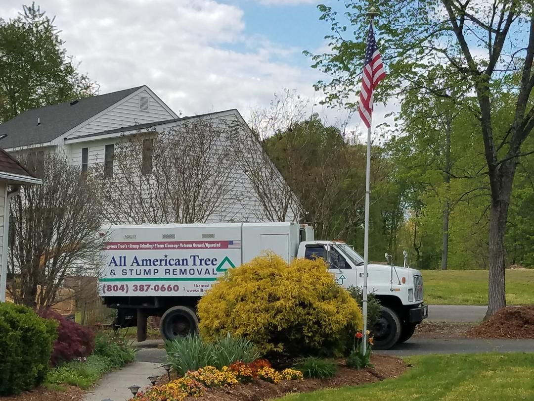 White All American Tree truck parked by a house with an American flag and landscaping