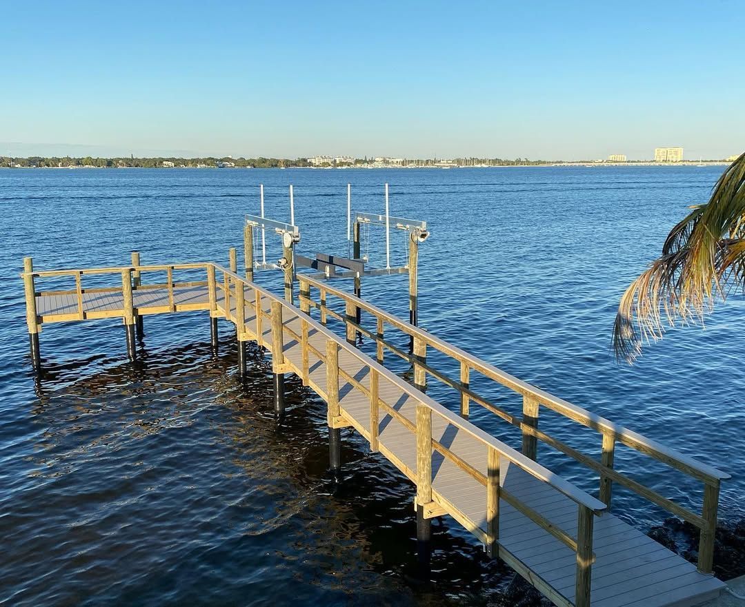 A wooden dock with a railing extending into a calm blue lake under a clear, bright sky.