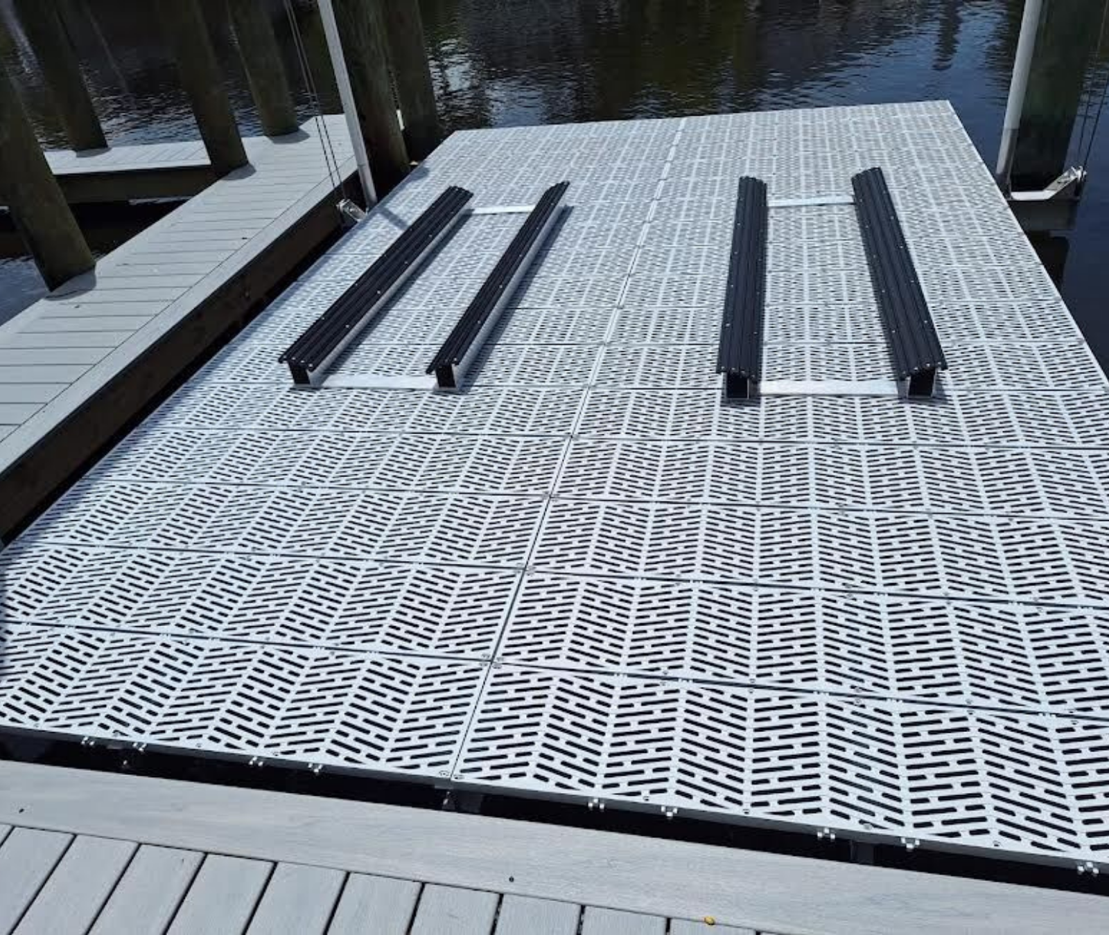A light gray floating dock with four black boat support rails installed on its textured, grid-patterned surface.