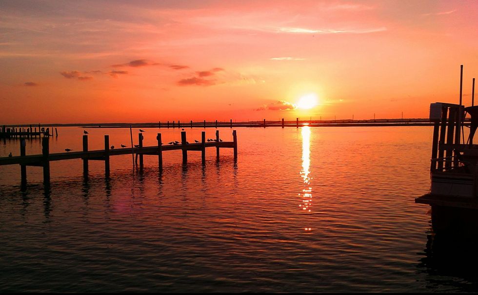 Sunset over calm water with silhouetted docks and a glowing orange reflection