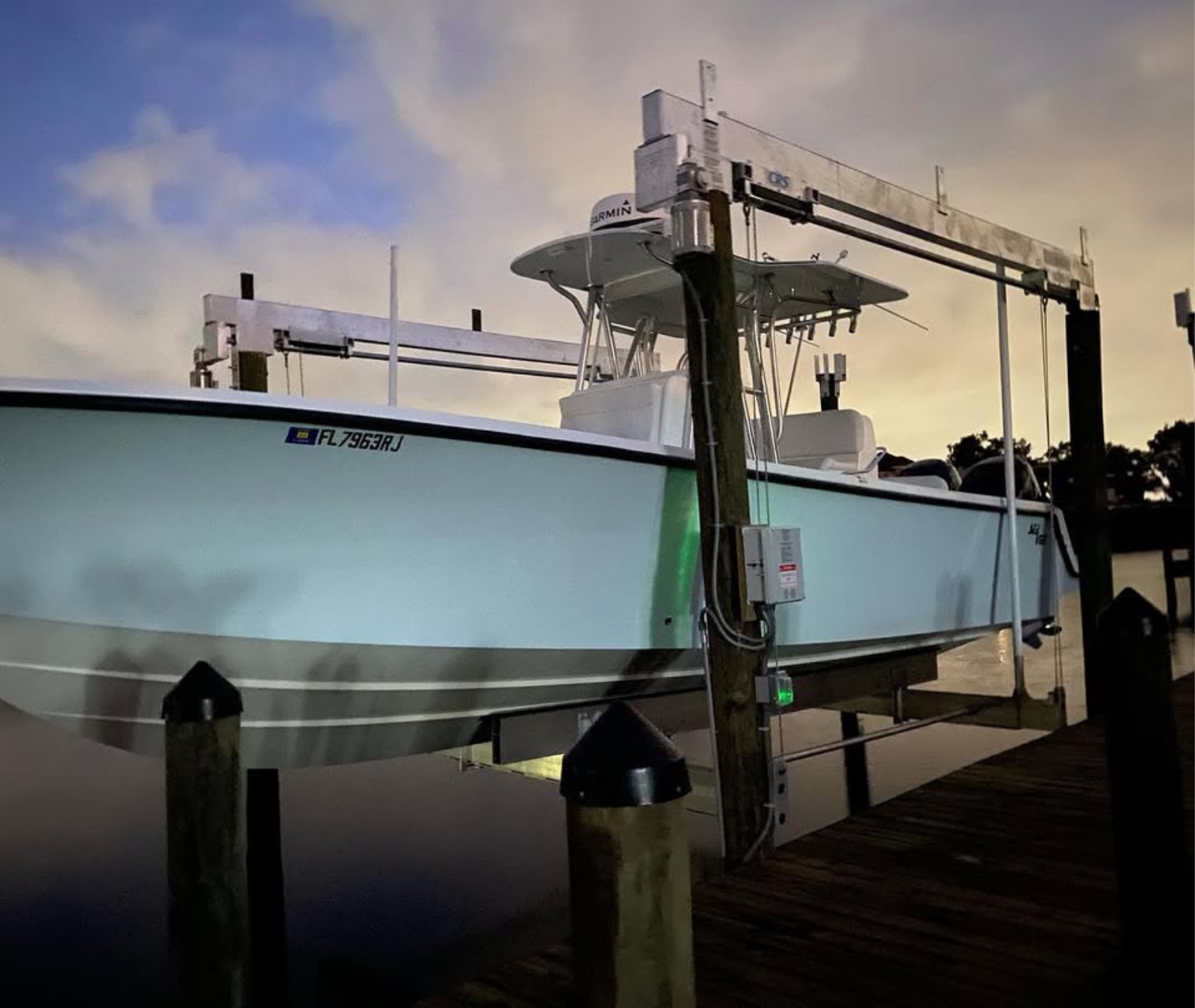 A light blue motorboat suspended on a lift above calm water at twilight.